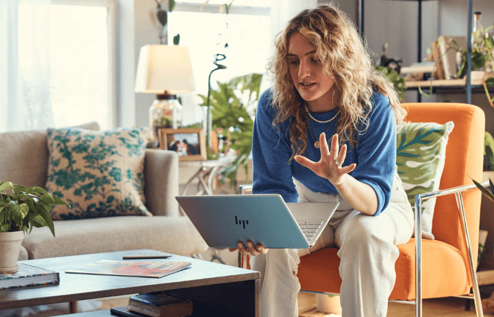 A woman having a virtual conference on her HP Spectre x360 laptop while sitting in an orange couch.